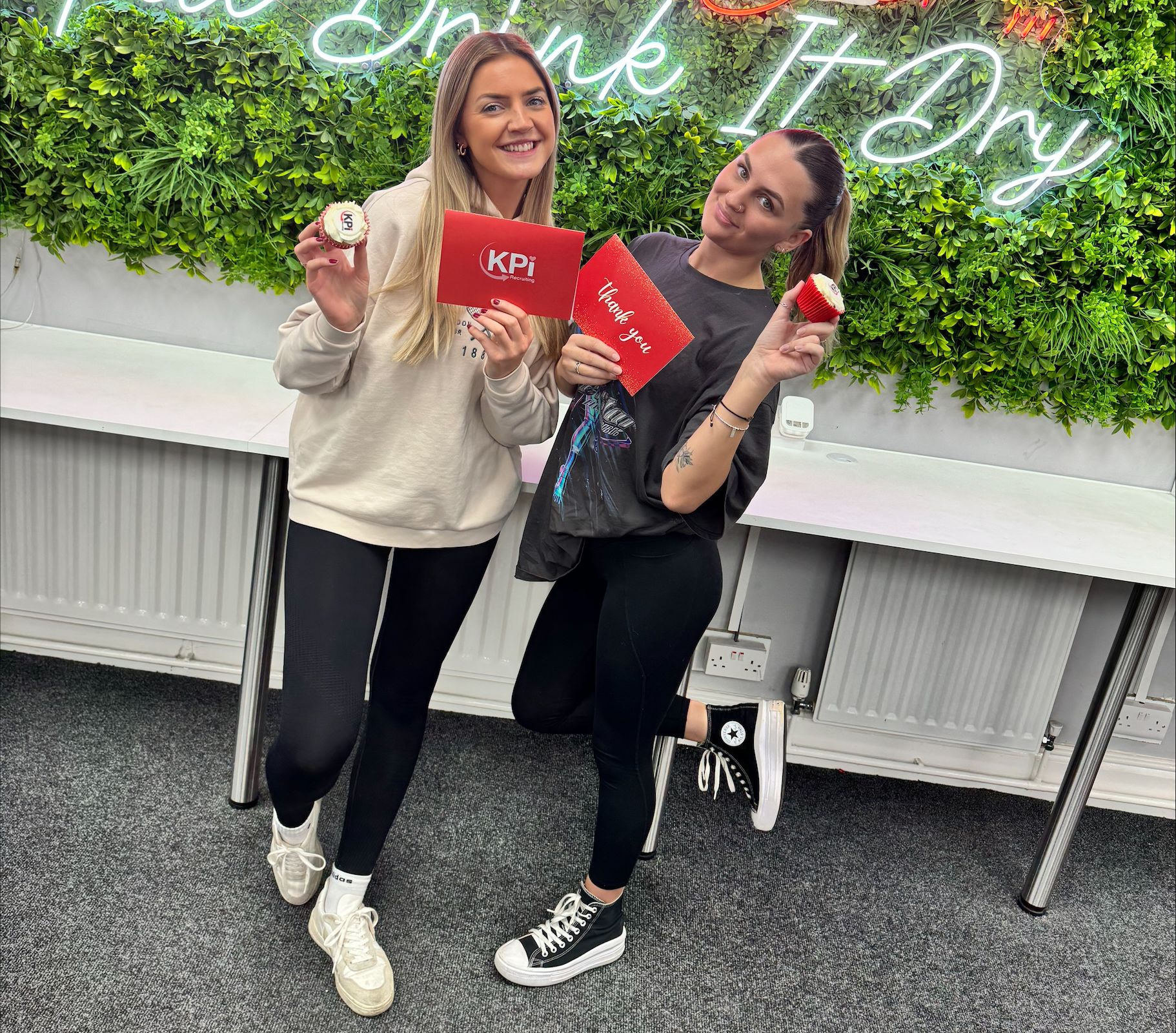 2 smiling women holding a cupcake and envelope.