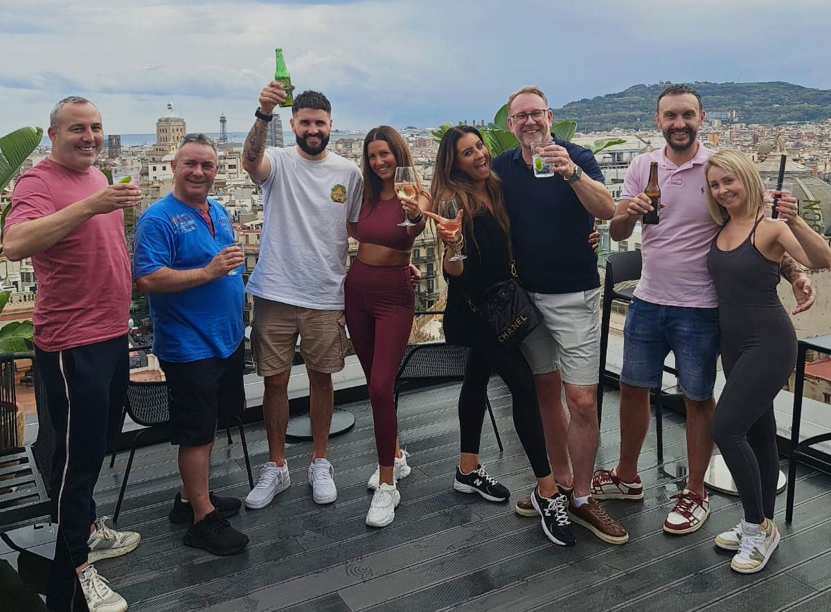 Group photo smiling holding drinks on a balcony.