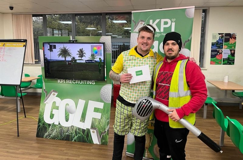 2 smiling men in front of a golf simulator