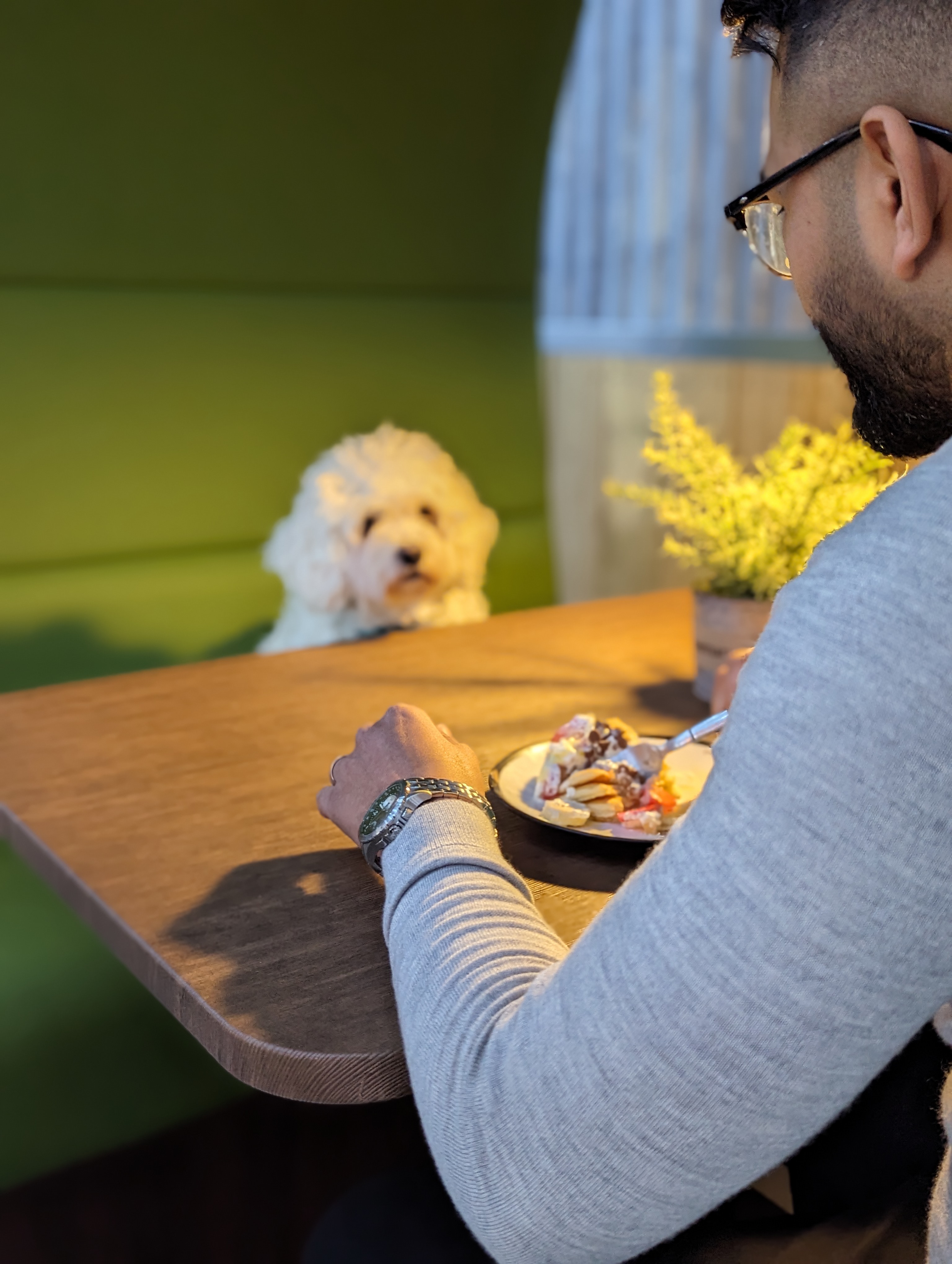 A man eating pancakes while a dog watches across the table.