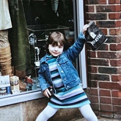 Picture of a young girl smiling at the camera outside of a shop.