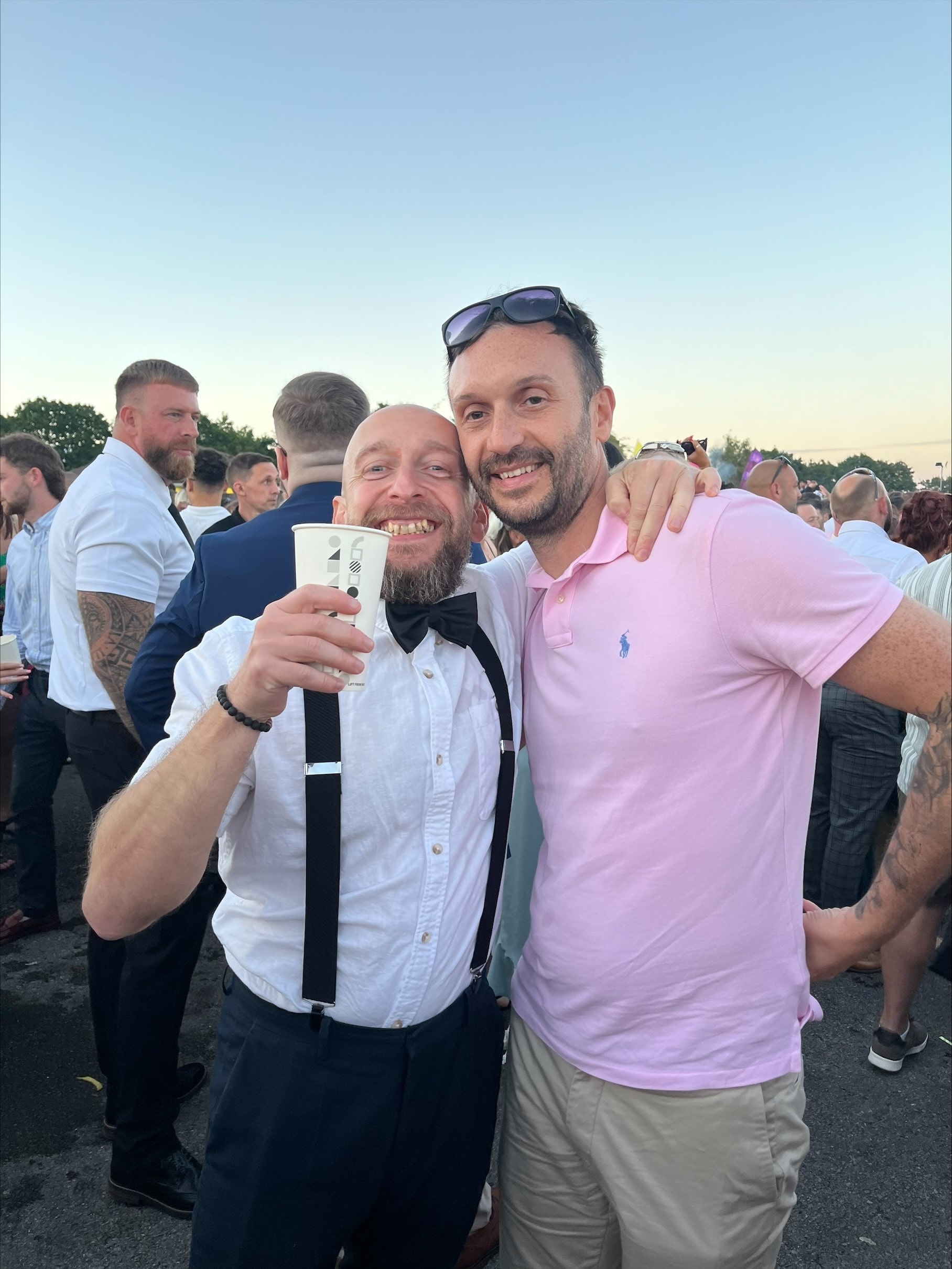 2 friends smiling at the races, one holding a drink.