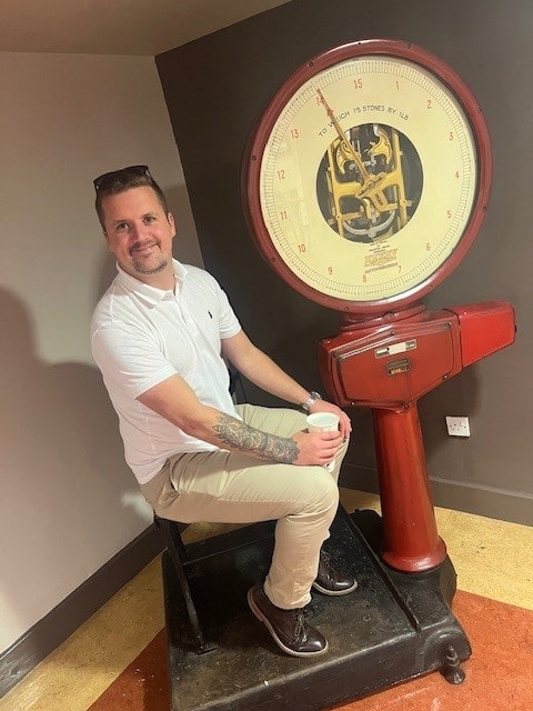 A male smiling, sat on an antique chair.